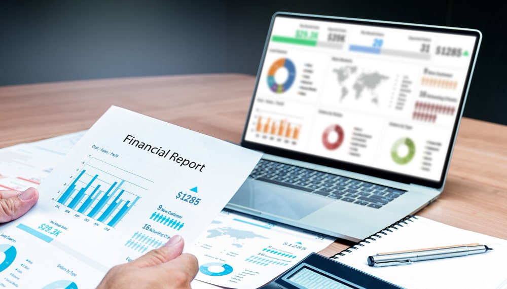 businessman-hand-holding-financial-report-document-with-mock-up-chart-presentation-display-laptop